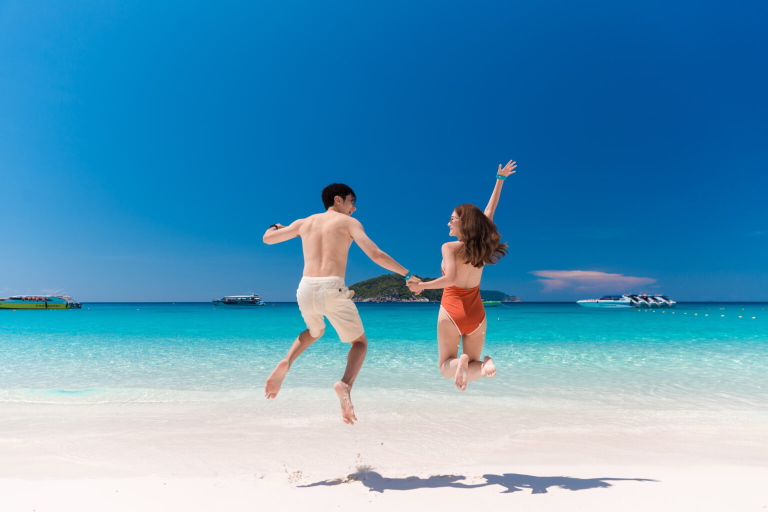 couple holding hand while jumping on a beach.